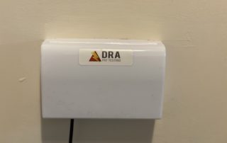 Double socket protected with a latched socket cover, with a DRA PAT Testing sticker on