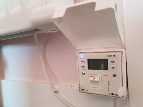 An open socket cover over a timer switch for a fan system on a pink wall