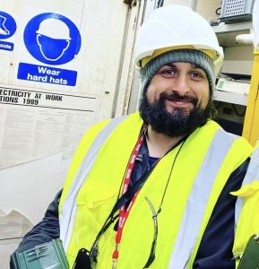 Rob Traynor PAT Tester, pictured in a hard hat and hi-vis whilst working on a ship